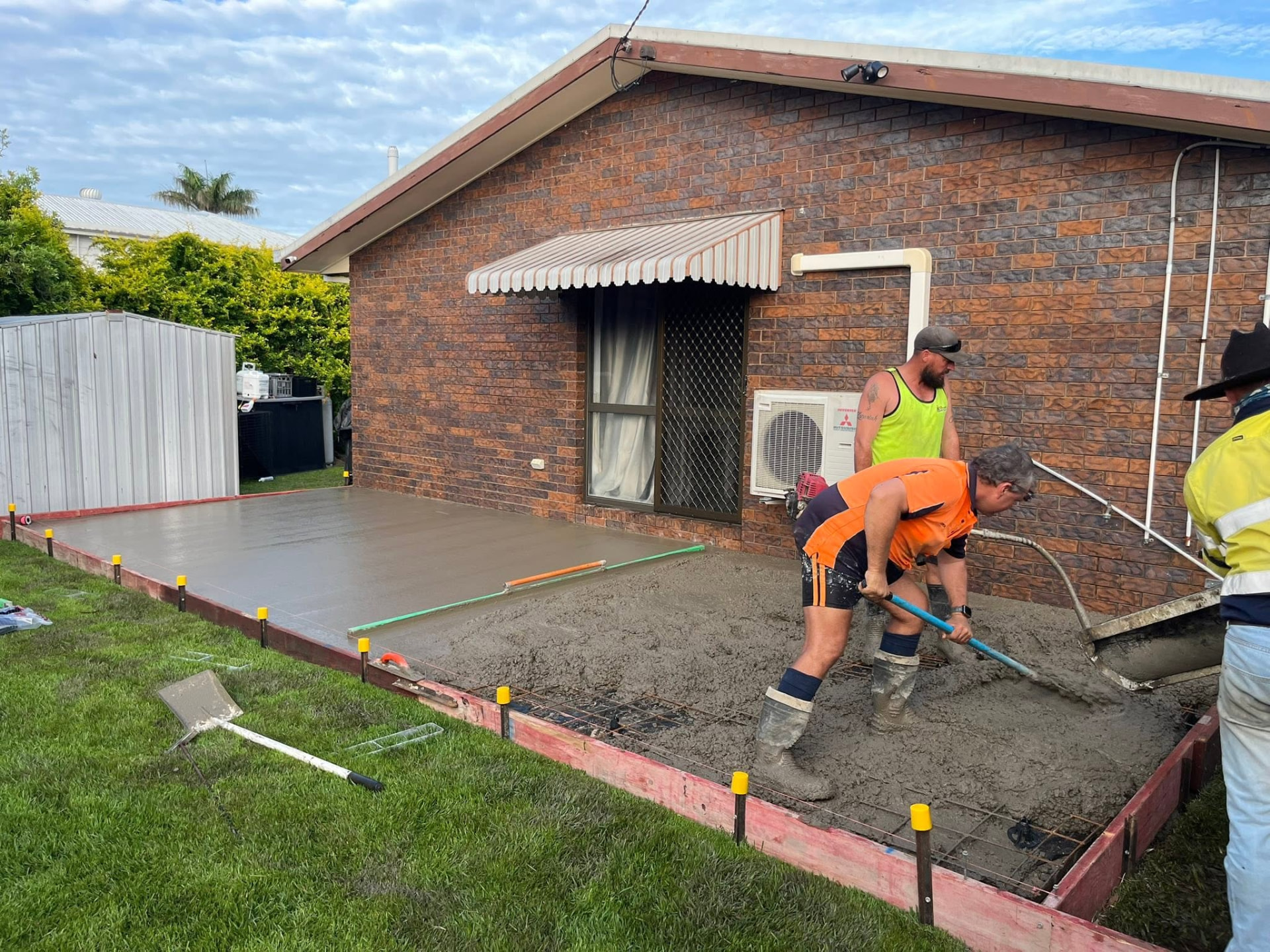 Crew screeding a freshly poured concrete slab beside a brick home in Mackay