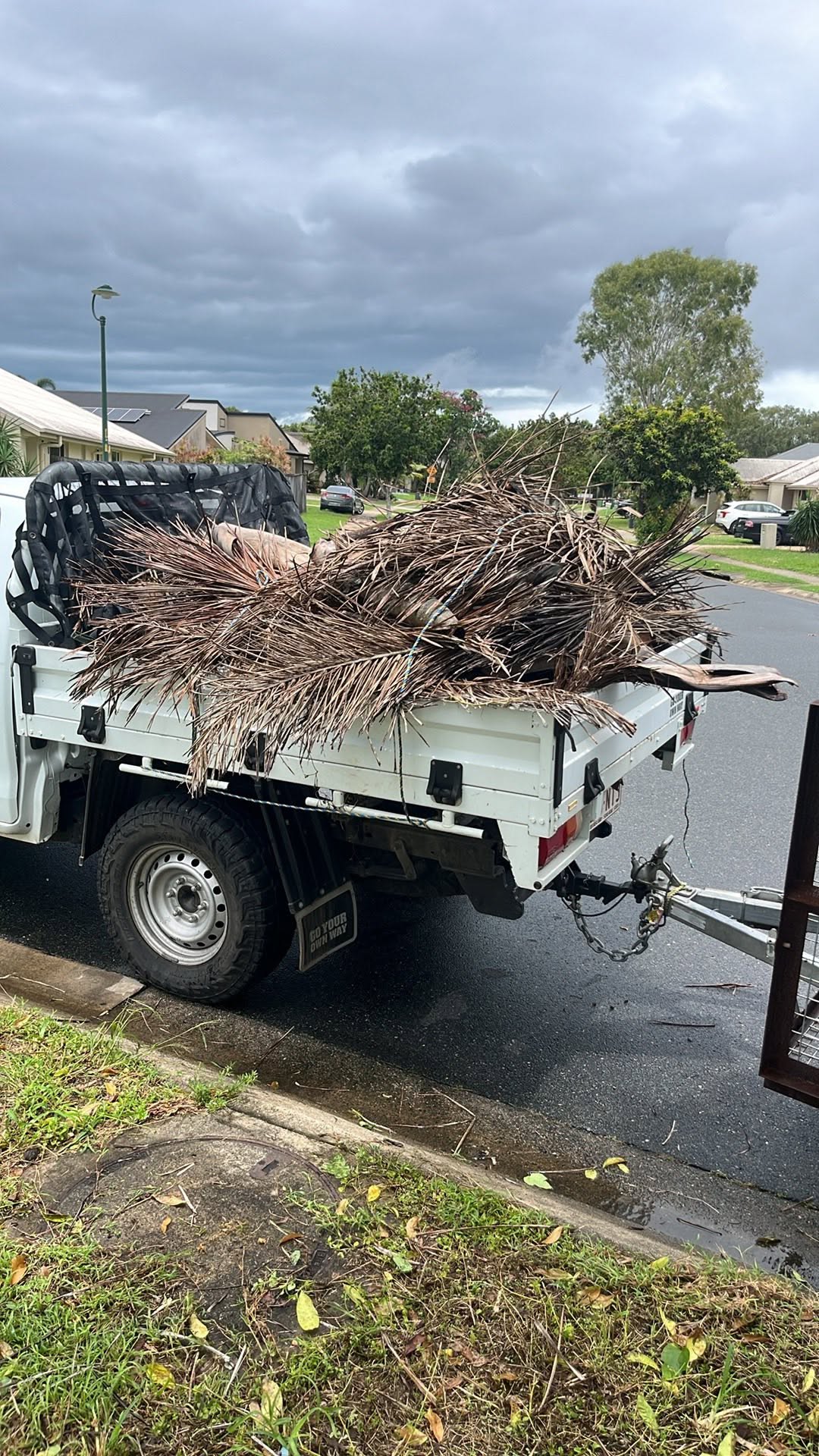 Ute trailer loaded with garden clippings and green waste bags in a driveway